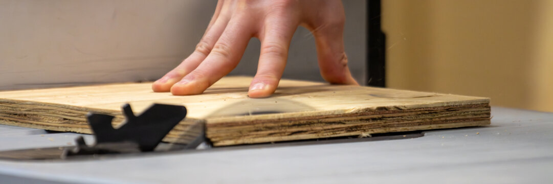 Canada, 14 April 2026 : Person's hand guides plywood through a table saw blade during woodworking