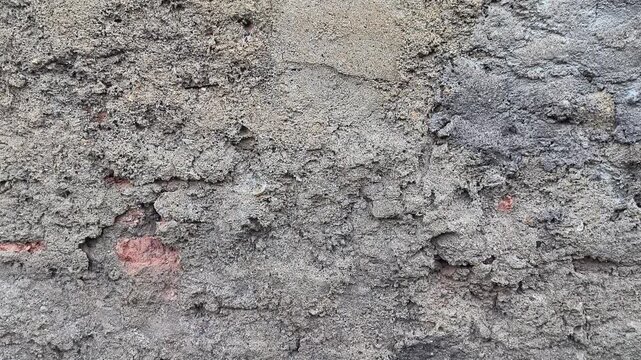 A close-up shot of a rough, weathered concrete wall with a crumbling plaster surface and exposed red brick fragments, creating a rustic industrial background