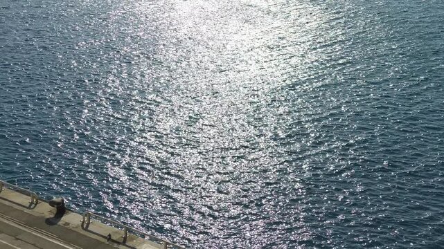 Lone person strolling along a waterfront promenade next to the sparkling Mediterranean Sea in France