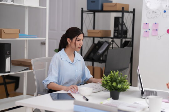 Medium shot of young Asian businesswoman, solo desk work in a modern office, open-plan desk area with metal, company staff, work life, Asia, clean airy workspace, small business and startup