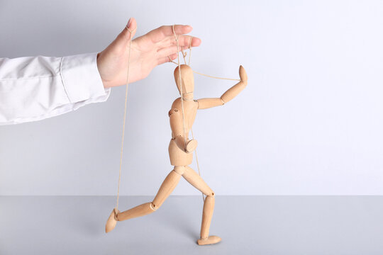 Hand of puppeteer manipulating marionette on light background