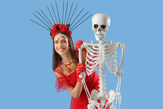 Beautiful young happy woman dressed for Halloween with skeleton on blue background