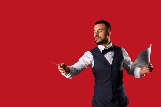 Young male conductor with note sheet on red background