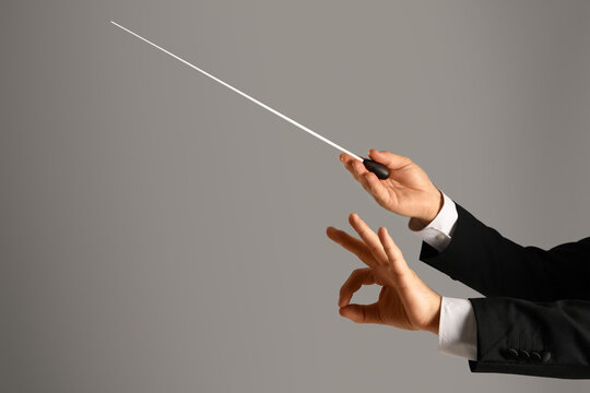 Hands of male conductor with baton showing OK on grey background