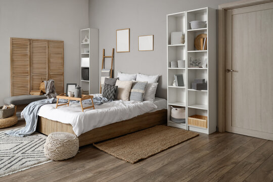 Interior of stylish bedroom with ladder, folding screen and shelf units