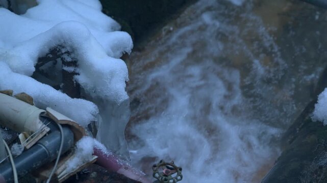 雪と氷に覆われた配管から激しく流れ出る温泉のスローモーション