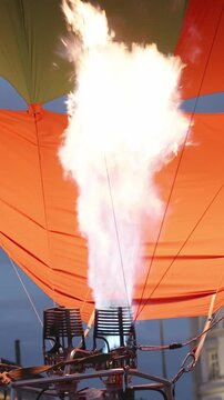 Vertical screen. Hot air balloon burner releases flames, lighting up the vibrant canopy as the balloon gets ready for takeoff in the evening sky