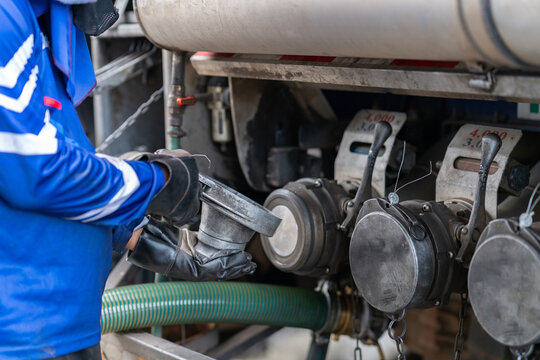 Fuel tanker driver in protective gloves connecting a discharge hose coupling to the truck valve at a petrol station