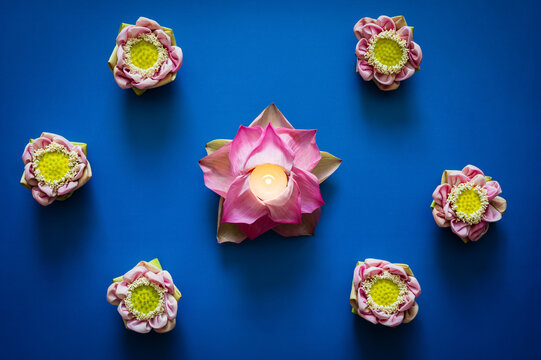 Diwali festival flat lay with glowing candle inside lotus flower on blue background.