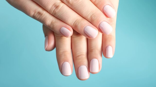 Female hands with pink manicure on blue background.