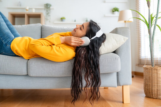 Portrait of Asian woman relaxing listening audio with headphones sitting on a couch at home