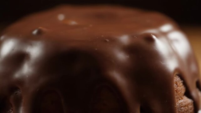 Macro close-up of decadent dark chocolate ganache frosting slowly dripping down the moist surface of a rich chocolate cake against a dark background.