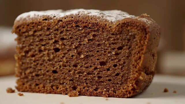 Extreme close-up of a slice of dark moist cake or gingerbread dusted with white powdered sugar, showcasing the porous texture of the baked dessert crumb.