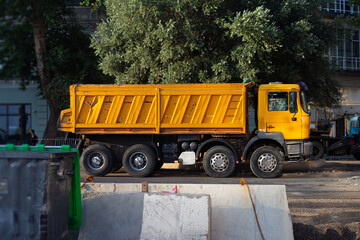 Street city photo. Large yellow dump truck with pebbles, crushed rock, gravel, ground, sand in back parked on construction site, heavy duty transport vehicle side view. Repair road work, build, job © brajianni