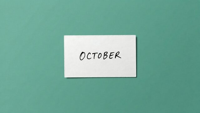 White rectangular card with the word october written in black handwritten script on a solid green background