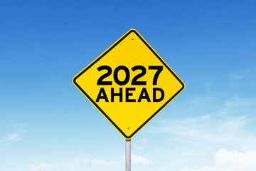Yellow Warning Road Sign with 2027 Ahead Text Against Blue Sky Concept © Creativa Images