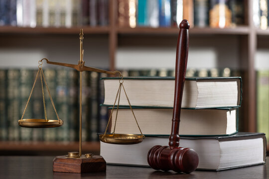 A judge's gavel and the scales of justice against a background of books and a bookshelf.