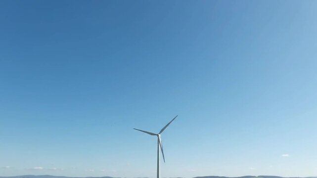 White wind turbine generating clean renewable energy against a clear blue sky