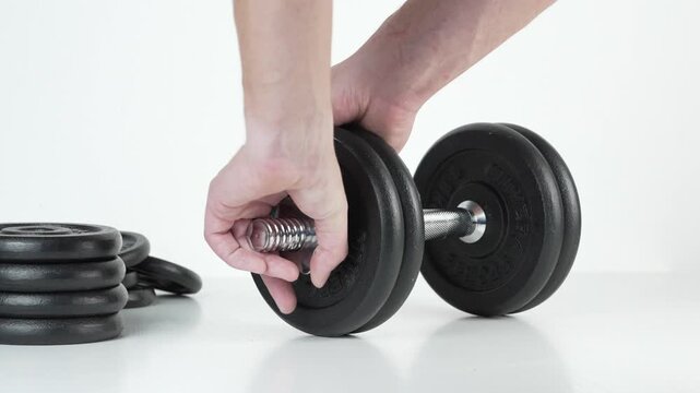 Hands adding weight plates to an adjustable dumbbell and securing screw collars on a white background