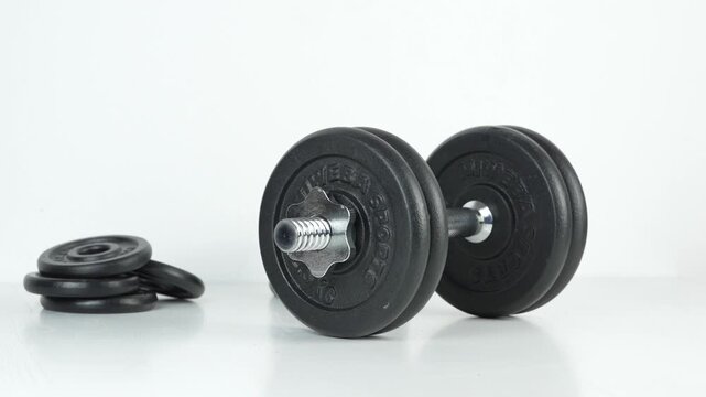 Adjustable dumbbell rolling into frame beside stacked weight plates on a clean white background
