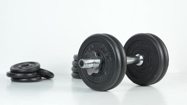 Hand placing an adjustable dumbbell in front of stacked weight plates on a white background