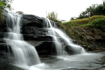 Beautiful tiered waterfall cascading over dark rocks in tropical nature © habibie