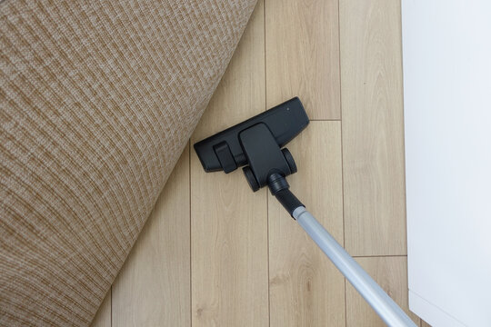A vacuum cleaner is currently being utilized on a wooden floor that has a rug placed on it