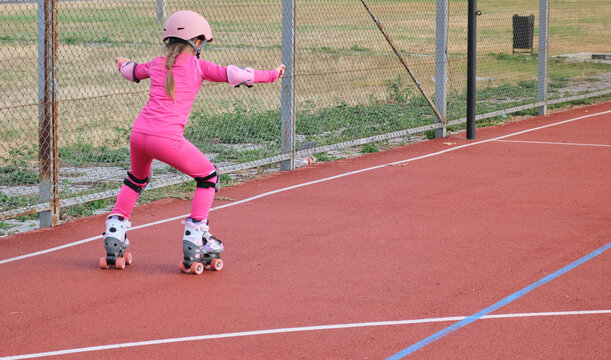 Girl practicing roller skating on a track in a fenced area during daytime