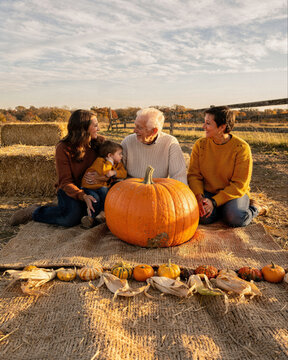 Multigenerational Family Sitting with Pumpkin in Autumn Field