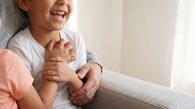 Close up of cheerful child laughing while sitting with parents on sofa, happy boy smiling and bonding with family at home, joyful family lifestyle and copy space background