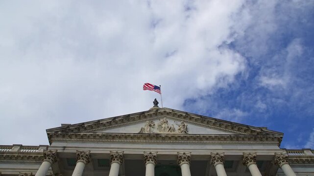 American flag waving on Capitol architecture. American flag in clouds over landmark US Capitol. American flag symbol of Amerika liberty. American flag on historic Capitol dome in Washington DC.