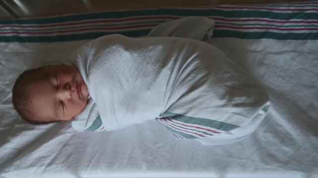 Swaddled newborn baby sleeping peacefully in hospital bassinet