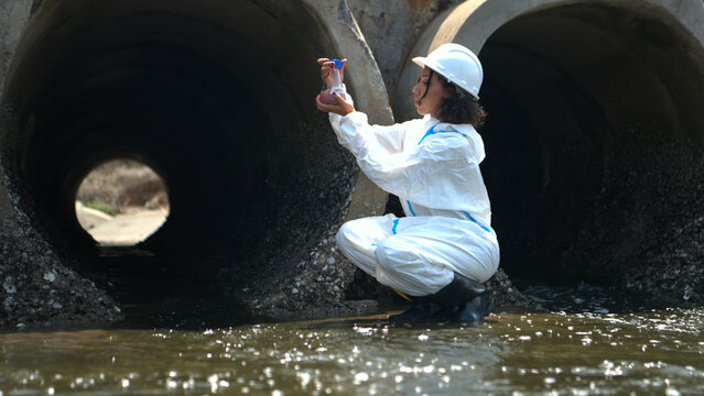 Environmental inspector in protective suit examining wastewater drainage system and industrial water pollution