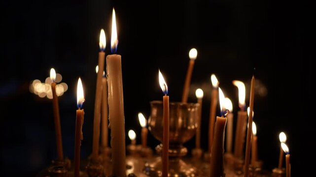 Many thin beeswax candles burning on a circular metal stand inside a dark church interior
