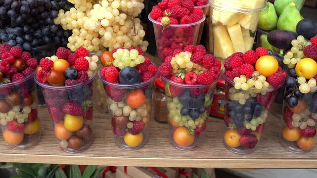 Assorted fresh fruit cups with berries and grapes arranged on a wooden table for catering events