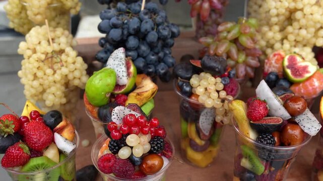 Assorted fresh fruit cups with berries and grapes arranged on a wooden table for catering events