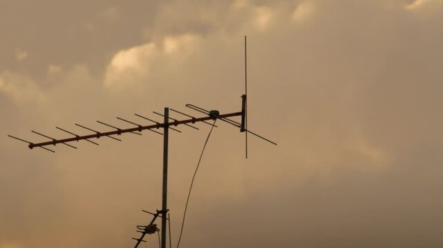 Silhouette of Rooftop TV Antennas Against Vivid Orange Sunset Sky