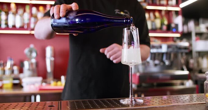 Pouring wine. Bartender service. Man hand adding sparkling bubble white blanc liquid from blue bottle to stemmed glass on counter.