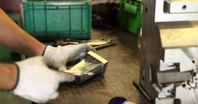 Close-up of gloved hands using a small rotary grinding tool to finish a metal component on a workbench. The scene highlights precision surface finishing, mold tooling