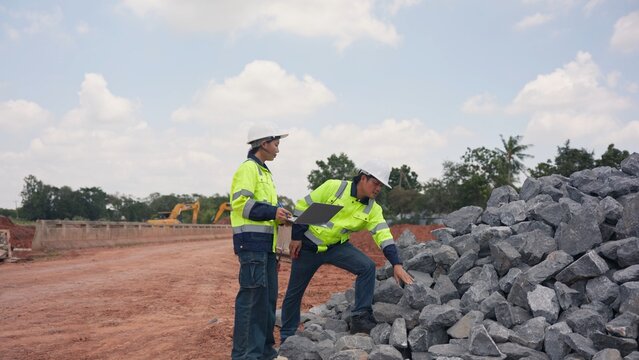 Asian male and female engineers checking riprap stone pile for erosion control at bridge site. Civil infrastructure development, soil protection and engineering teamwork concept.