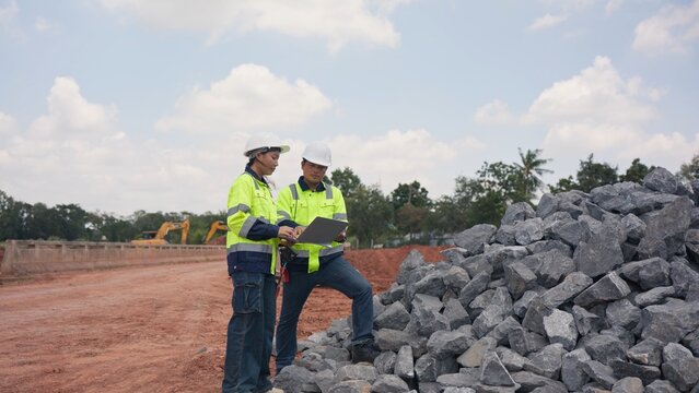 Asian male and female engineers checking riprap stone pile for erosion control at bridge site. Civil infrastructure development, soil protection and engineering teamwork concept.