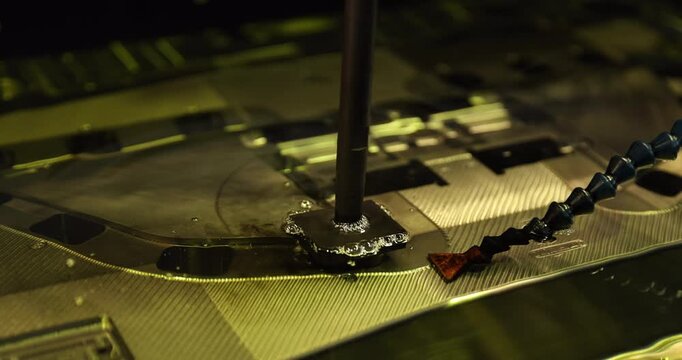 Close-up of industrial mold manufacturing, showing a vertical tool positioned over a metal workpiece with fluid and bubbles around the working area.
