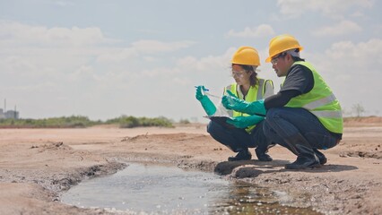 Obraz premium Asian male and female environmental inspectors kneeling by puddle to inspect water and soil pollution near factory. Environmental surveillance, ecological study and testing concept.