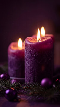 Close-up vertical shot of burning purple candles with glowing flames, surrounded by fir tree branches and shiny violet Christmas baubles in a dark setting.