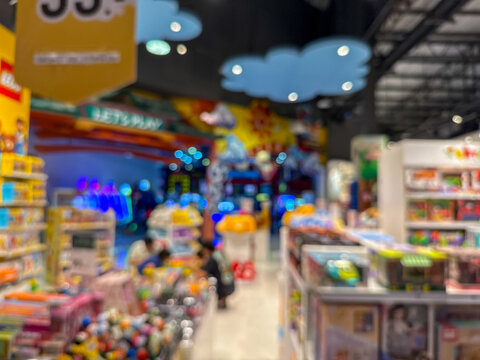 Blurred image of people walking down a wide, well-lit corridor in a modern shopping mall or large retail center, with colorful bokeh lights.