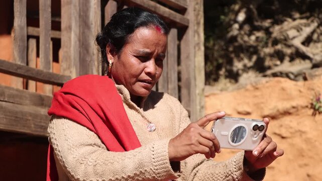 A rural village woman is looking at a modern smartphone outdoors next to a house