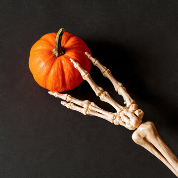 A bony skeleton hand reaching out for a vibrant orange pumpkin in a darkened setting Generative AI