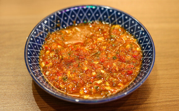 Freshly ground spicy chili sambal served in a blue patterned ceramic bowl on a wooden tabletop.