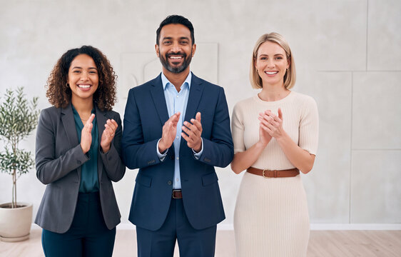 Group of business people smiling and clapping hands while standing in a bright modern office