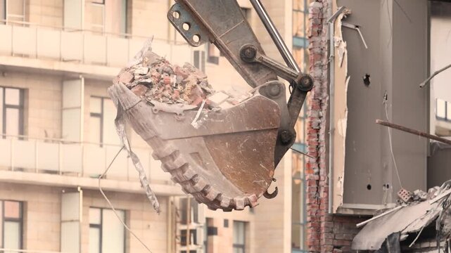 Excavator bucket lifts rubble near partly demolished apartment block